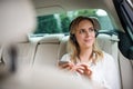 Business woman with smartphone and headphones sitting on back seats in taxi car. Royalty Free Stock Photo