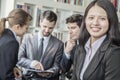 Business woman smiling and looking at the camera with her colleagues talking and looking down at a digital tablet in the Royalty Free Stock Photo