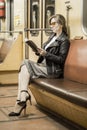 Business woman in a subway car reads a book. Beautiful girl in sunglasses and a jacket in a subway car. Fashionable and stylish Royalty Free Stock Photo