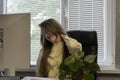 Business woman suffers from pain in her neck while sitting at her workplace. Woman works in office and kneads her neck