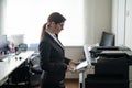 Business woman in a suit and glasses makes copies of documents on a photocopier. Female office manager is doing paper Royalty Free Stock Photo