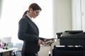 Business woman in a suit and glasses makes copies of documents on a photocopier. Female office manager is doing paper Royalty Free Stock Photo