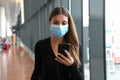 Business woman with surgical mask and mobile phone looks for flight at the airport