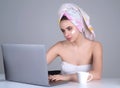 Business woman with towel on head facial cream on face hold cup of coffee working on laptop. Morning beauty. Portrait of