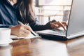 Business woman using laptop and writing on a notepad with a pen at a coffee shop. Working on project concept Royalty Free Stock Photo