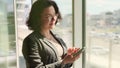 Business woman using a mobile phone in the office near the window. Smartphone texting, typing text messages on mobile phone checki