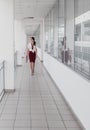 Business Woman Walking Along the Office Corridor. Smiling Businesswoman Goes Against White Offices Background. A young pretty girl