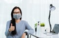 Business woman wearing face mask protective working from home office show finger thumber for good job sign Royalty Free Stock Photo