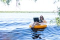 Business woman working on a laptop in an inflatable ring on the river, the concept of working on vacation. Royalty Free Stock Photo