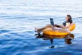 Business woman working on a laptop in an inflatable ring on the sea, the concept of working on vacation. Royalty Free Stock Photo