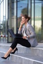 Business woman working on laptop and phone in front of office building Royalty Free Stock Photo