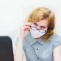 A business woman works from home in a protective mask, wears glasses.