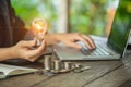 Business women hand holding light bulb on stack coins and working with computer on workplace. Creative ideas concept of saving mon Royalty Free Stock Photo