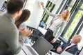 Business woman showing scheme on chartboard to colleagues at meeting room.