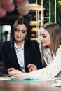 Business women in smart casual wear are discussing affairs, drinking coffee and smiling while co-working in the cafe