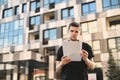 A business young man in a black shirt stands with papers in his hands and reads on the background of modern architecture. Serious Royalty Free Stock Photo