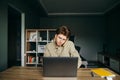 Business young man in a shirt working on a laptop at his desk at home and talking on the phone with a serious face. Busy employee Royalty Free Stock Photo