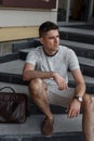 Business young man in a stylish summer striped T-shirt in fashionable shorts in suede shoes with a leather bag sits