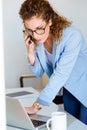 Business young woman talking on the mobile phone while using her laptop in the office. Royalty Free Stock Photo