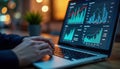Businessman analyzing sales data on laptop. Hands on keyboard. Graphs, charts displayed on screen. Nighttime setting. Focus on