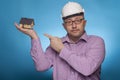 A businessman, architect in a piked shirt and hard hat pointing with the index finger on a house