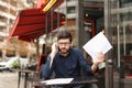 Businessman arguing by smartphone and reading papers at cafe tab