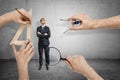 Businessman, arms folded, standing and looking up, and four big hands around measuring him with magnifying glass