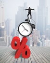 Businessman balancing on alarm clock and red percentage sign