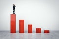 Businessman with binoculars standing on top of red chart made of wooden bricks on light background. Crisis, finance and business