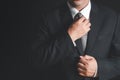 Businessman with black suit adjusting his necktie on black background Royalty Free Stock Photo