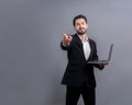 Businessman in black suit holding laptop pointing finger at camera. Fervent Royalty Free Stock Photo