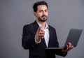 Businessman in black suit holding laptop pointing finger at camera. Fervent Royalty Free Stock Photo