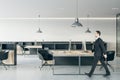 Businessman in black suit walking through wooden work table with modern computers in open space modern office with dark stylish Royalty Free Stock Photo