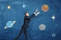 Businessman on blue chalkboard background trying to grasp a drawn planet among many others.