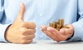 Businessman in blue shirt holds in his hand lot of coins. Positive thumbs up, like. Royalty Free Stock Photo