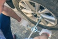 A businessman in a blue suit using cross wrench tighten the bolts wheel of punctured wheel. Hole in the tire. Concept.