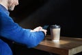 Businessman in blue sweater drinks coffee in a sunny cafe, close-up holds a disposable paper glass, using smartphone while having Royalty Free Stock Photo