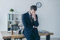 Businessman with bowed and closed eyes touching face while standing at workplace