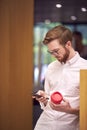 Businessman On Break In Office Holding Re-Usable Coffee Cup And Looking At Mobile Phone