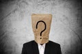 Businessman with brown paper bag on head, with question mark, on concrete texture background Royalty Free Stock Photo