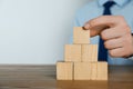 Businessman building pyramid of blank cubes on table against light background, closeup. Space for text Royalty Free Stock Photo