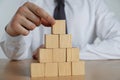 Businessman building pyramid of blank cubes on wooden table. Space for text Royalty Free Stock Photo