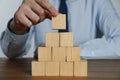 Businessman building pyramid of blank cubes on wooden table, closeup. Space for text Royalty Free Stock Photo