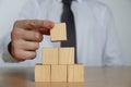 Businessman building pyramid of blank cubes on wooden table, closeup. Space for text Royalty Free Stock Photo