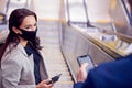 Businessman And Businesswoman Riding Escalator At Railway Station Wearing PPE Face Mask In Pandemic