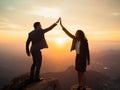 Businessman and businesswoman standing on cliff with arms raised up on mountain top at sunset. Royalty Free Stock Photo