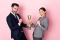 Businessman and businesswoman in suits holding trophy and gesturing on pink, gender equality concept
