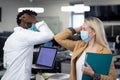 Businessman and businesswoman wearing face masks greeting each other by touch elbows at office