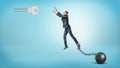 A businessman chained to an iron ball tries to jump and reach a large silver key hanging above.