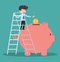 Businessman climb up on a ladder and putting coin into the piggy bank